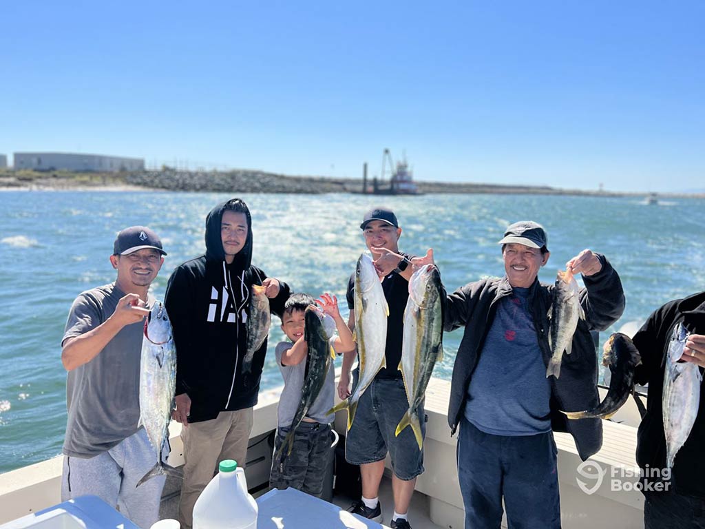 A group of male anglers of different generations smile as they show off their haul from a Huntington Beach fishing trip on a summer's day.