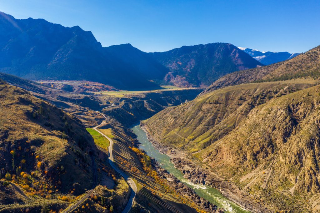 An aerial photo of the scenic Fraser River Canyon on a clear day, with the river narrowly working its way through the ridge in the center of the image.