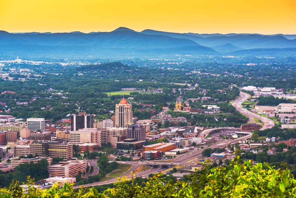 An aerial view of the city of Roanoke, with massive mountains in the background, and bright yellow skies at sunrise