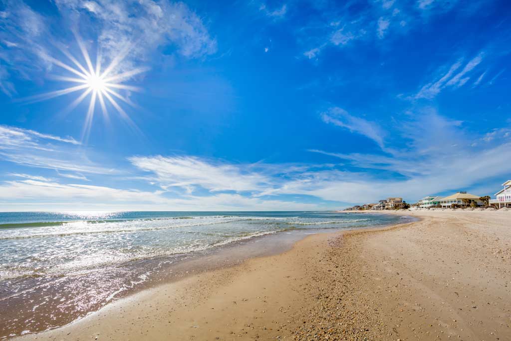 A view across a sandy beach at St. George Island, with clear skies, the surf, and beach houses in the distance