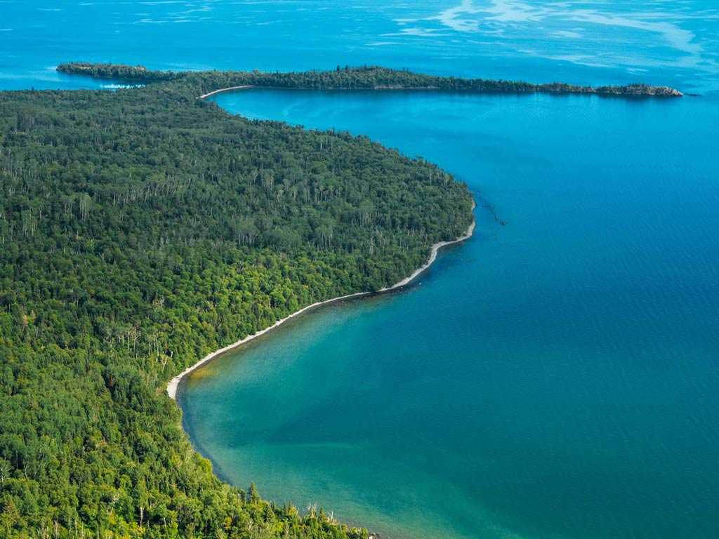 An aerial view of Lake Superior with its beautiful blue water posing against the greenery and shoreline on a bright and sunny day