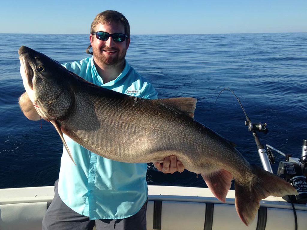 A photo of an angler standing on a charter boat and proudly showing off a big Lake Trout caught on a Michigan fishing trip
