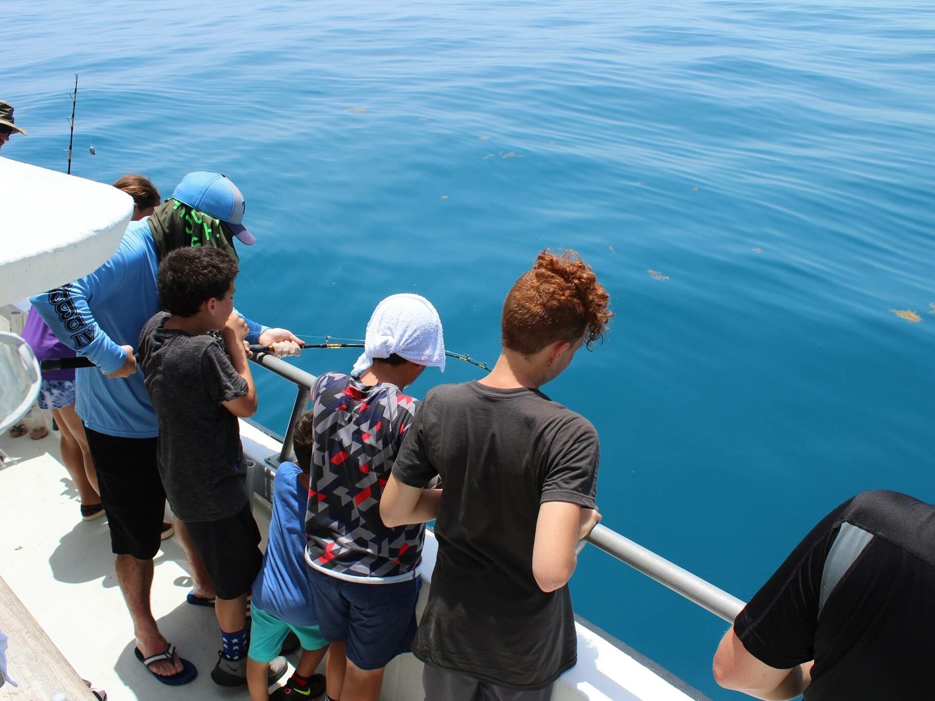 Kids fishing in Islamorada on a party boat with a crew member holding a rod and showing them how to bottom fish
