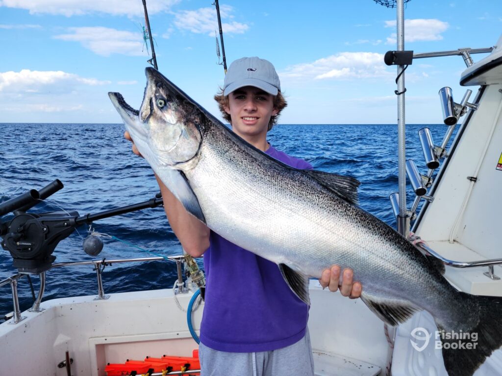 A teenager golding a large Salmon on a boat in one of the best US fishing states, with fishing rods visible in the background.