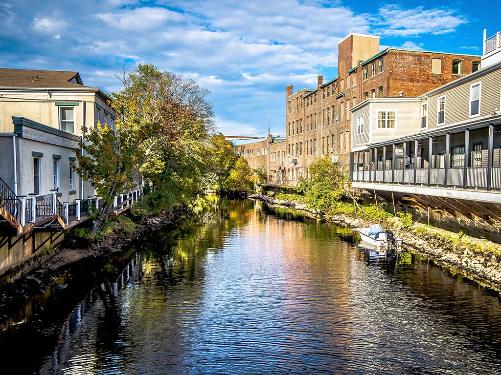 A view along a river or canal in Westerly, Rhode Island, on a sunny day, with houses on either sides of the waterway and a boat parked on the right of the image