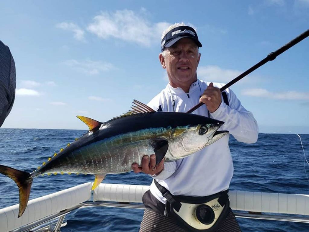 A photo of an angler wearing a cap while standing on a deep sea fishing charter and holding a decent Yellowfin Tuna catch
