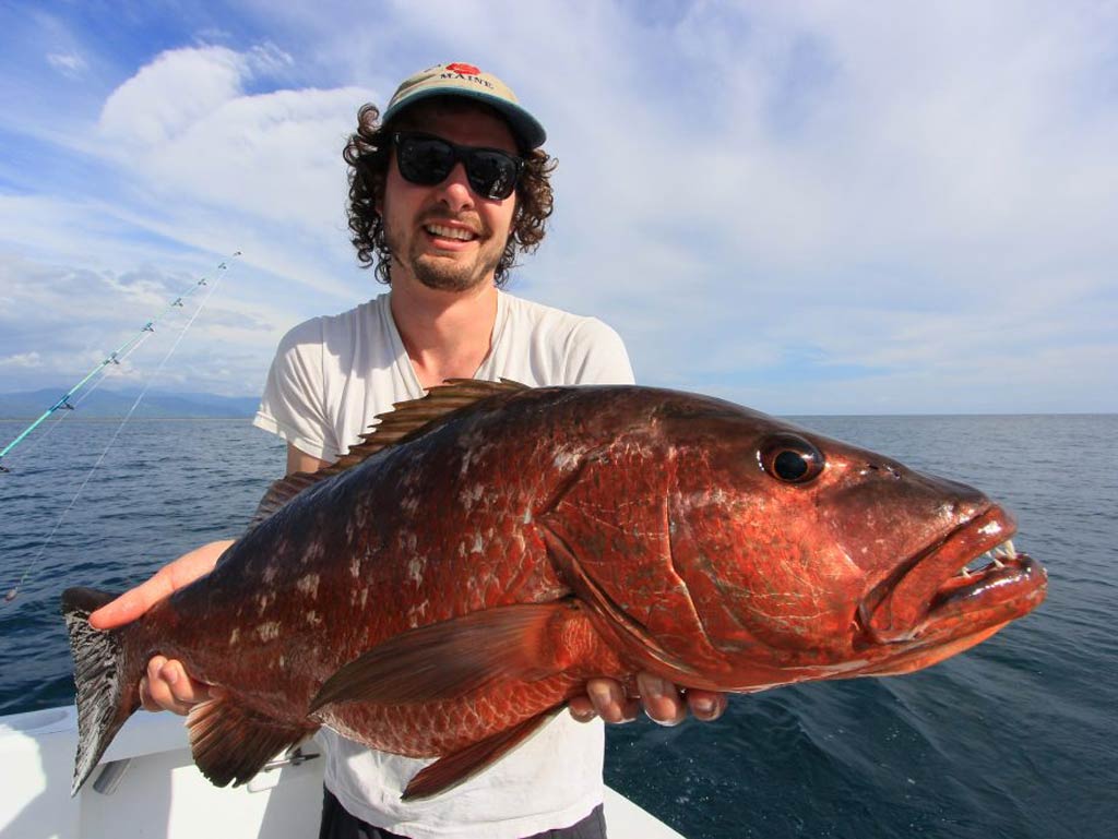 An angler standing on a charter fishing boat and posing with Cubera Snapper caught while deep sea fishing offshore