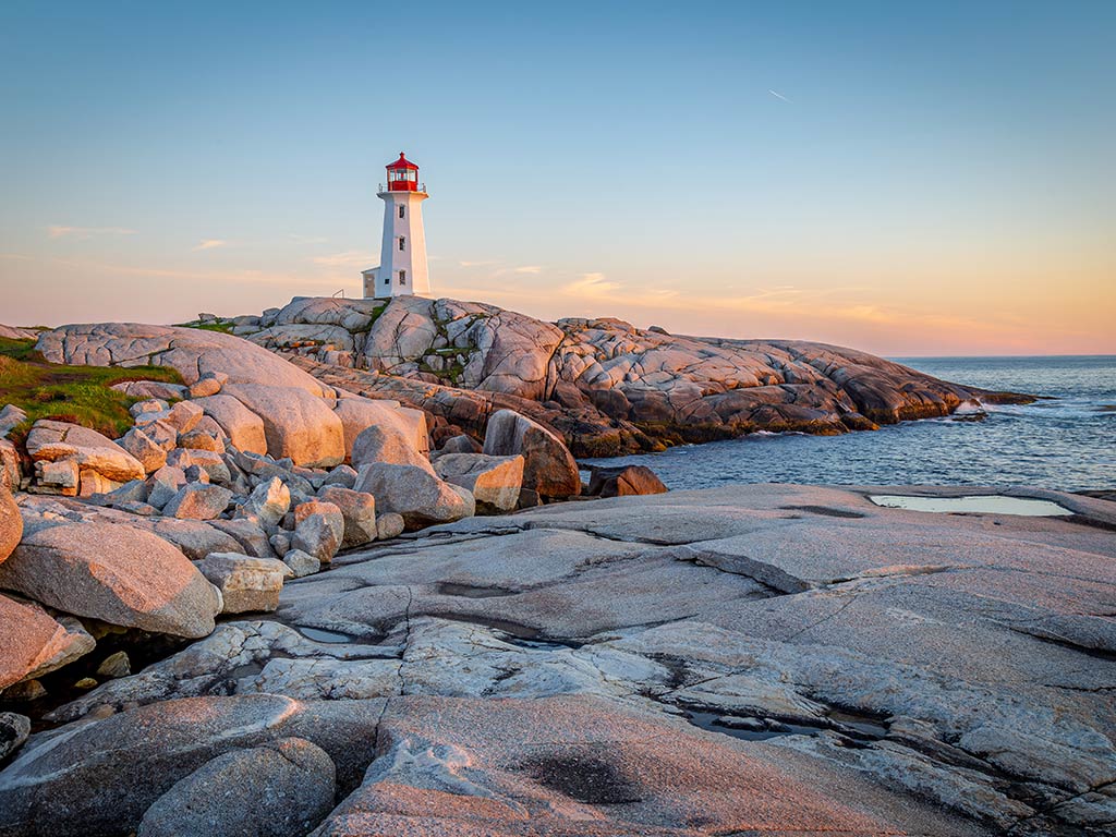 A view across a stony beach towards a lighthouse in Nova Scotia, Canada at sunset