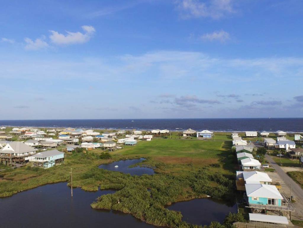 An aerial view of Grand Isle wetlands and houses, with the Gulf of Mexico/America visible in the distance.