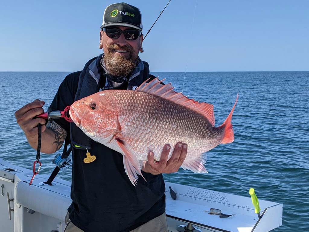 A smiling angler standing on a Louisiana charter fishing boat and holding a sizable Red Snapper with the ocean in the background.
