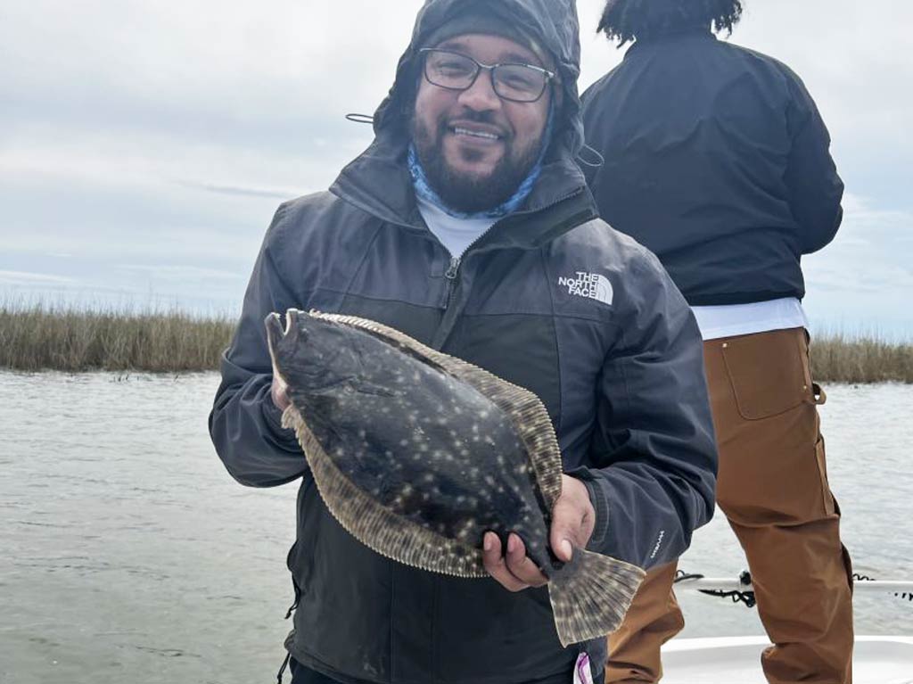 An angler standing on a charter fishing boat and holding Flounder caught while fishing in Louisiana on a cloudy and cold day.