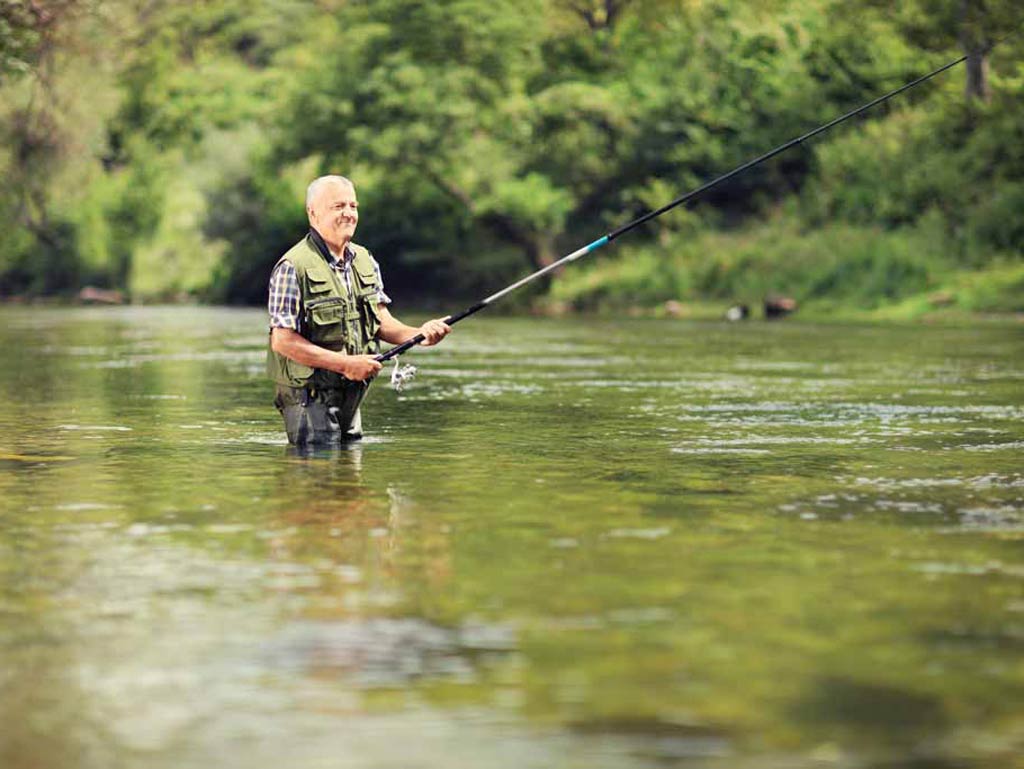 A photo of an angler wading while river fishing surrounded by green trees in murky waters