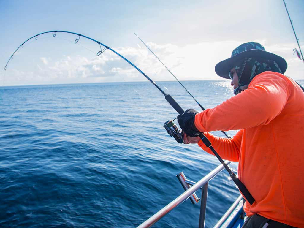 An angler wearing a long sleeve shirt, face mask, and a hat while deep sea fishing