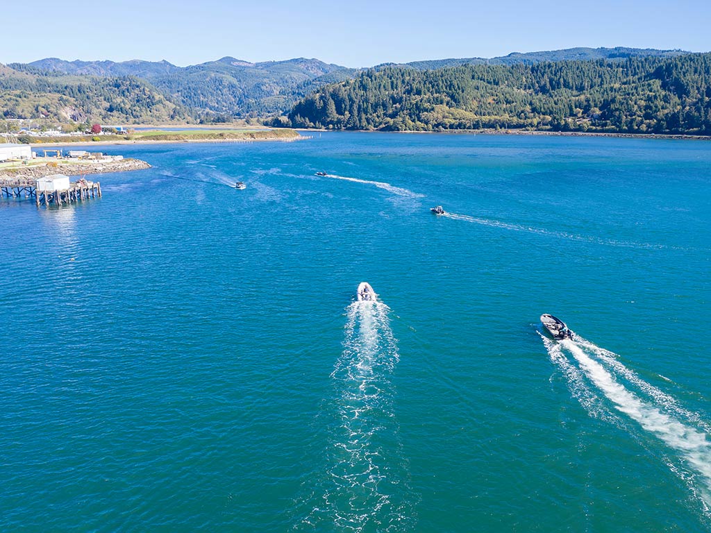 An aerial view looking towards Garibaldi, OR, with a number of fishing boats returning to the marina on a sunny day