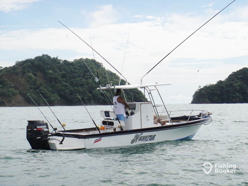 A view across the water towards a panga boat in Santa Cruz, Costa Rica, with downriggers and outriggers fitted for trolling the waters on a cloudy day