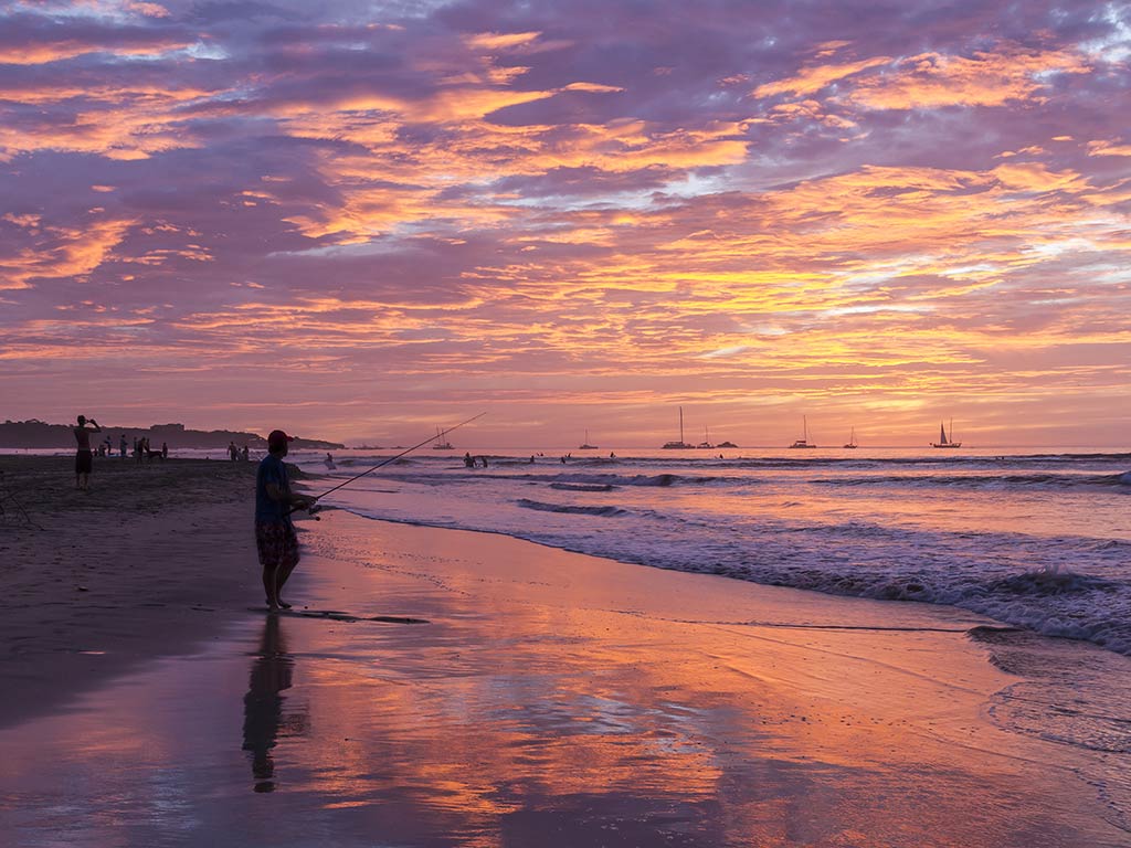 A view across a beach at sunset with a silhouette of a man fishing at sunset in Costa Rica with clouds setting in