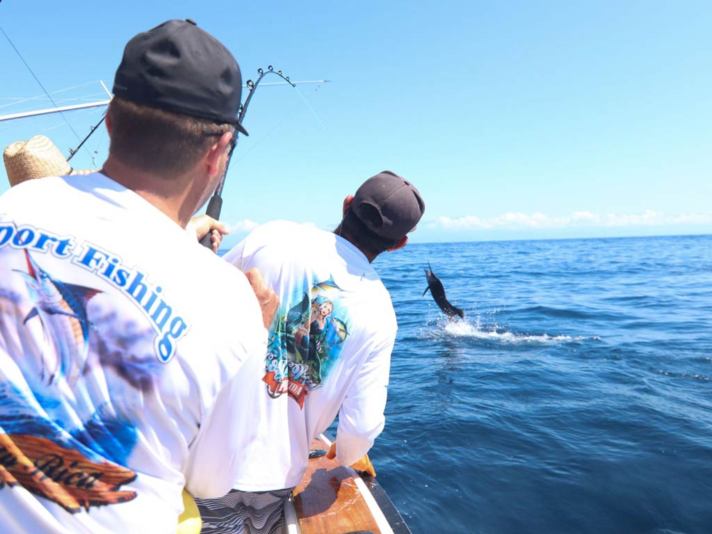 A photo of two anglers looking at Billfish leaping while they are trying to battle it during their deep sea fishing trip in Costa Rica