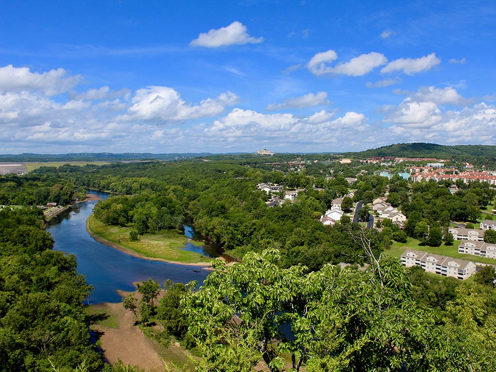 A view from a hill towards Table Rock Lake, near Branson, Missouri, on a clear day, with tree-lined shores and some buildings between them visible