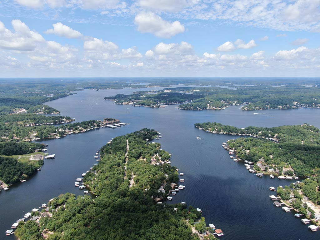 An aerial view of the Lake of the Ozark in Missouri on a day with sunny intervals, with green islands and outcrops visible in the foreground and distance