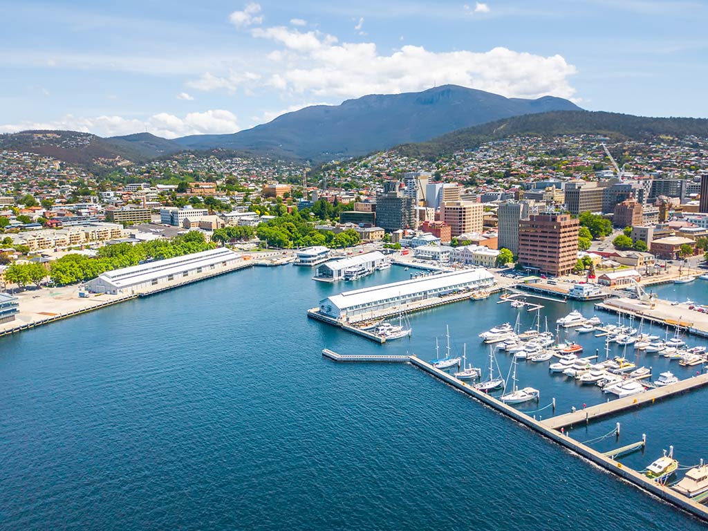 An aerial view of a harbor in Hobart, Tasmania, full of boats and fishing charters, with a mountain visible in the distance