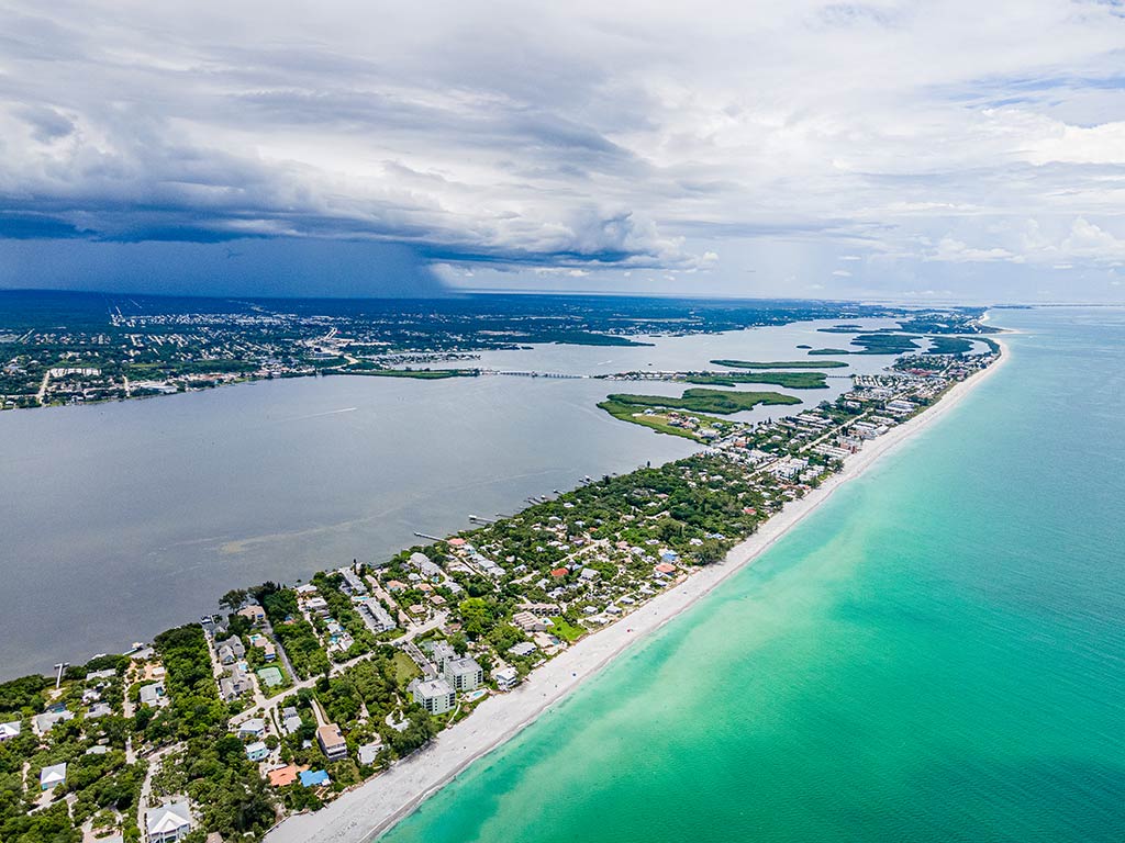 An aerial view of Boca Grande island with the Gulf of Mexico's turquoiuse waters on the right of the image, separated from the Tampa Bay on the left by a barrier island in the middle on a cloudy day