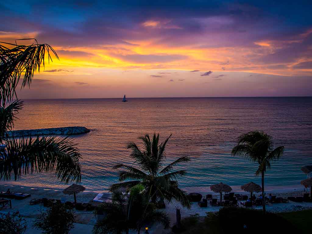 A view from a beach out to the waters of Montego Bay at sunset, with a blue-red hue in the sky