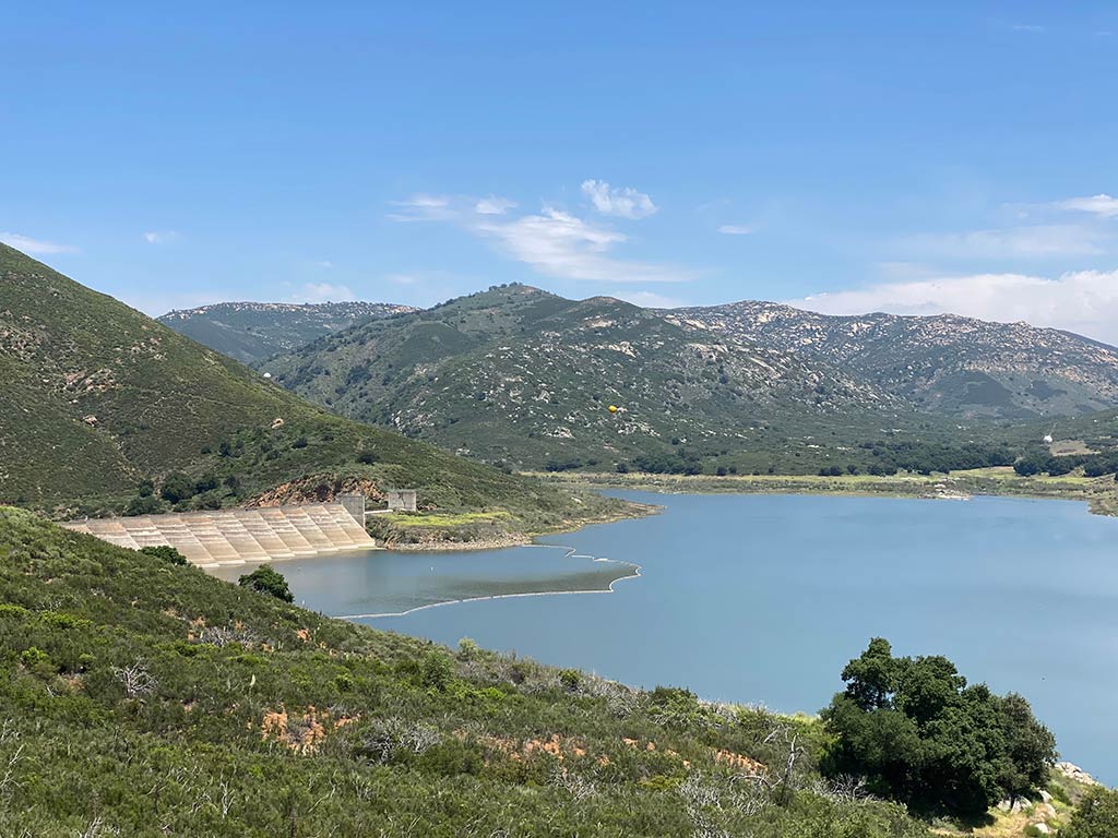 A view from a hill towards a dam in Sutherland Reservoir, Southern California, on a clear day, with hills visible in the distance