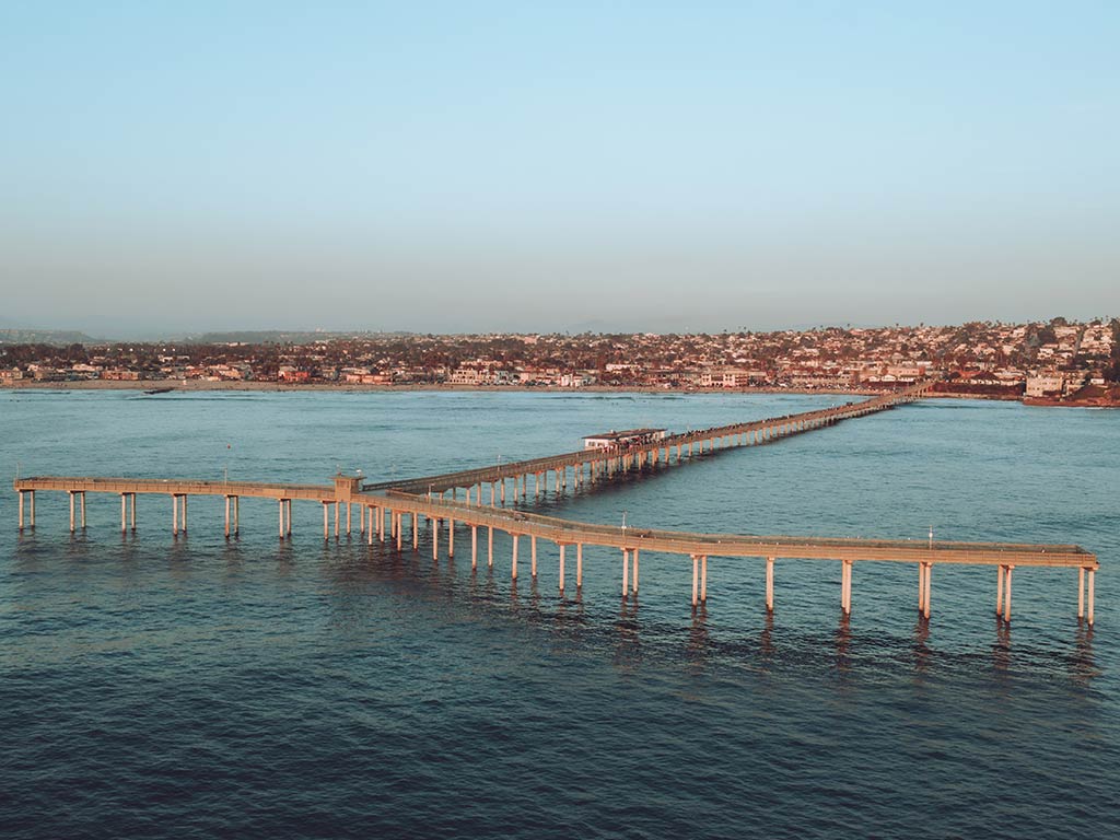 An aerial view of Ocean Beach fishing pier in San Diego, looking towards the city from the ocean at sunset on a clear day