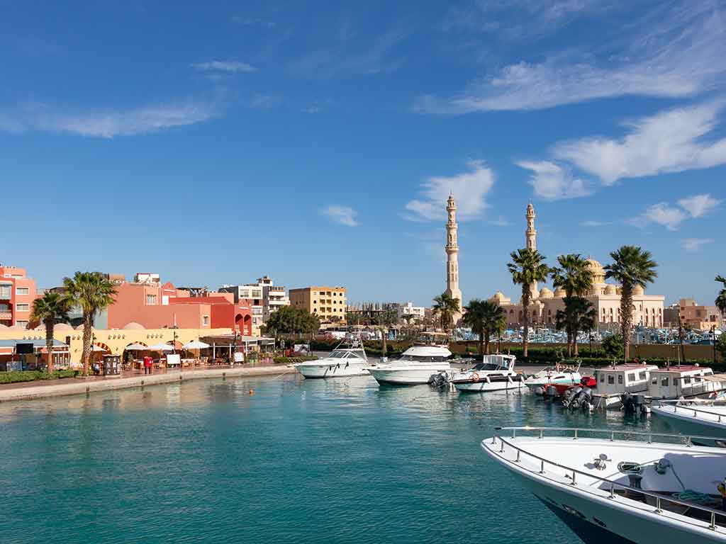 A view across the water towards a harbor and mosque in Hurghada, Egypt, with a few luxury boats visible in the foreground