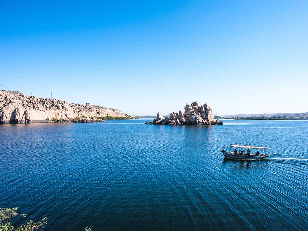 A view across the water of Lake Nasser towards some rocks in the middle of the lake on a clear day as a boat makes its way nearby