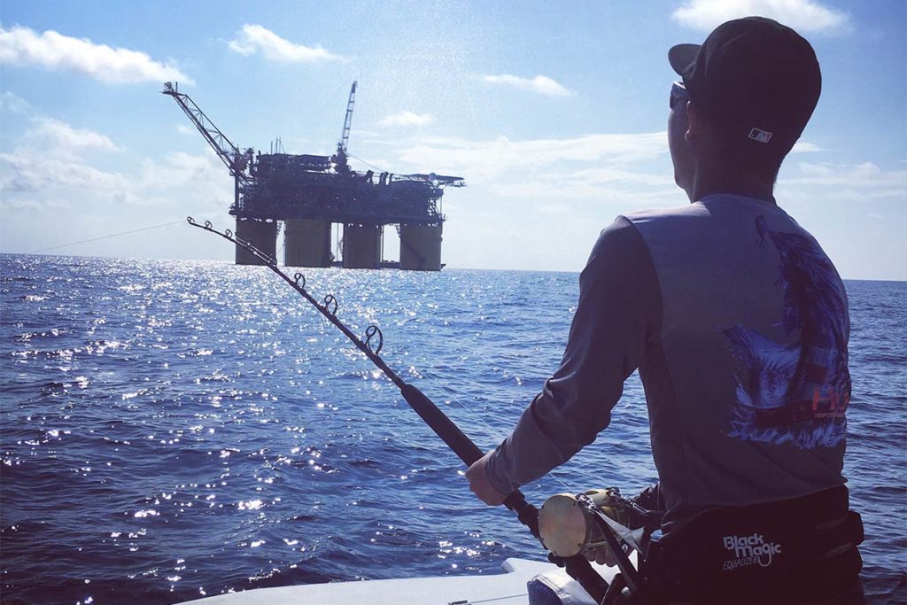 An view of an angler facing away from the camera while bottom fishing near an oil rig offshore in Alabama