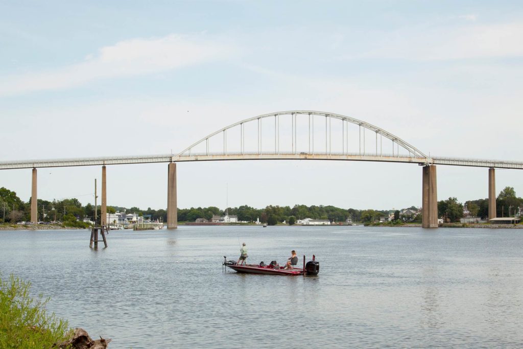 A small fishing boat makes its way along the Chesapeake Delaware Canal with a bridge in the background