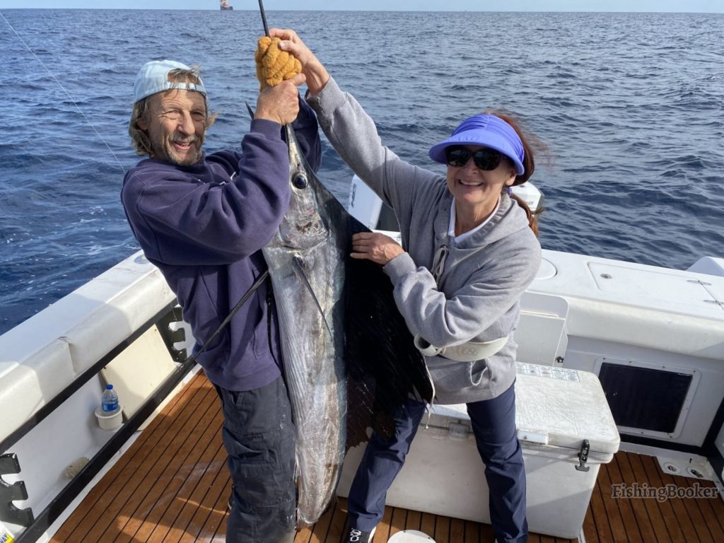 smiling anglers holding a Sailfish on a fishing boat