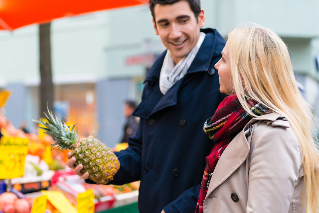A couple in a Farmers Market buying a pineapple.