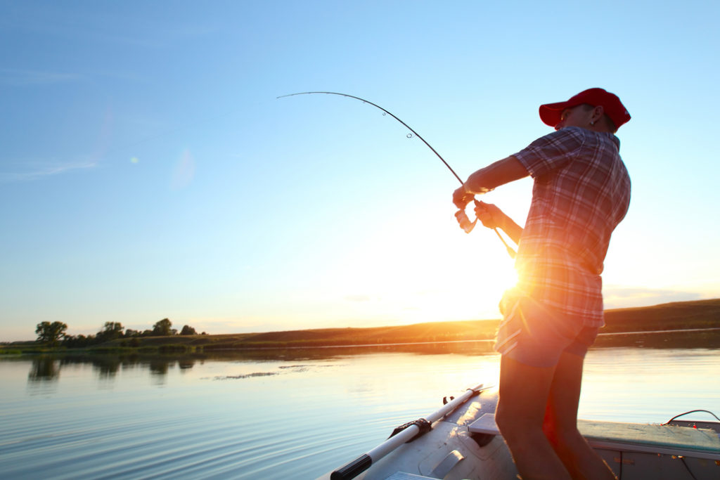 an angler fishing from a boat with the sun rising in the background