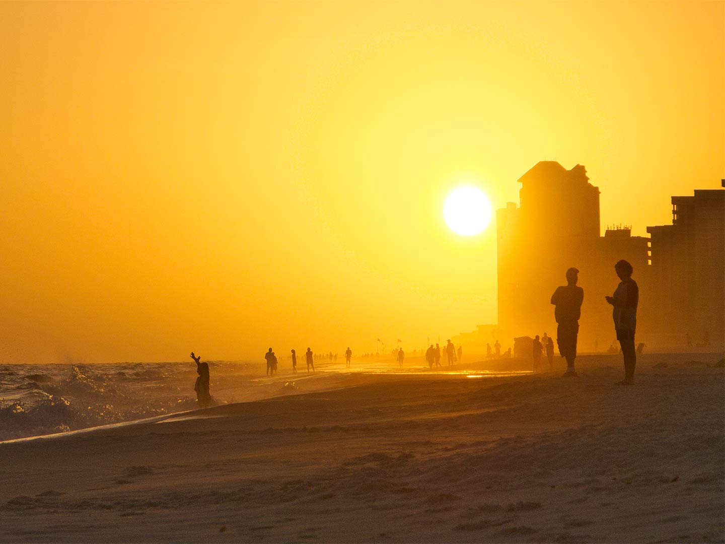 People enjoy the last of the day's sun on the beach in Orange Beach, with the sun dominating the background of the picture and turning the people into silhouettes