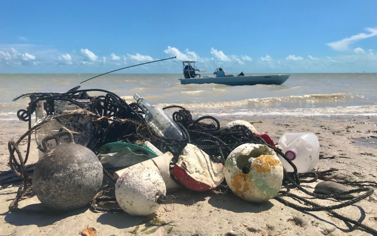 debris lying on a beach with a fishing boat and the ocean in the background