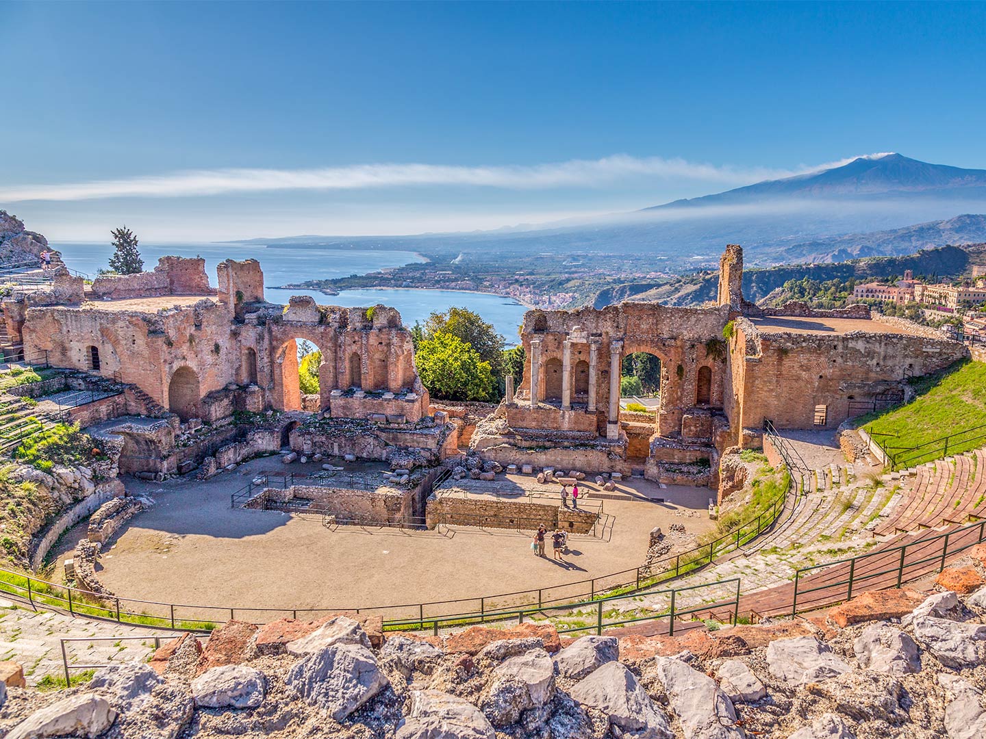 An aerial view of a Roman amphitheater in Taormina, Sicily, with Mount Etna in the background, Italy