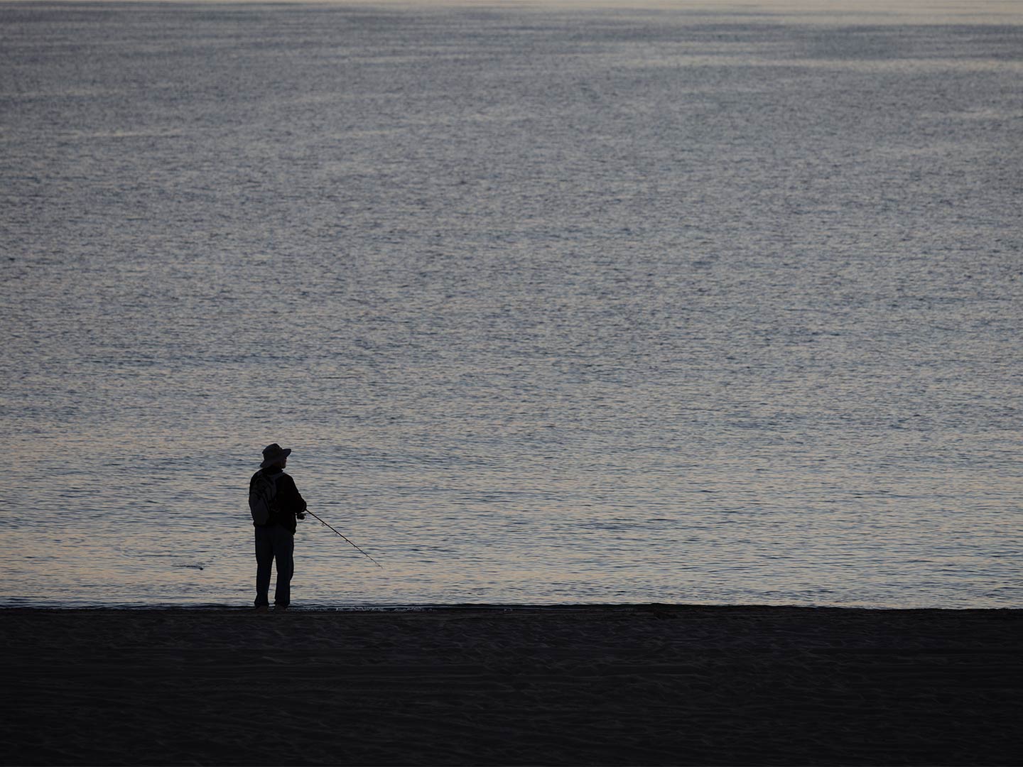 A lone angler stands on the beach, fishing from shore in the Sea of Cortez