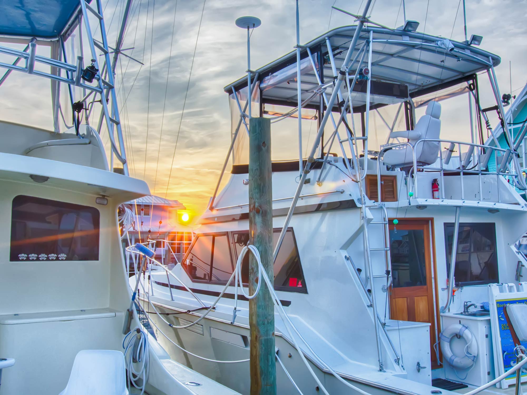 Two large sportfishing boats next to each other next to a dock at sunrise