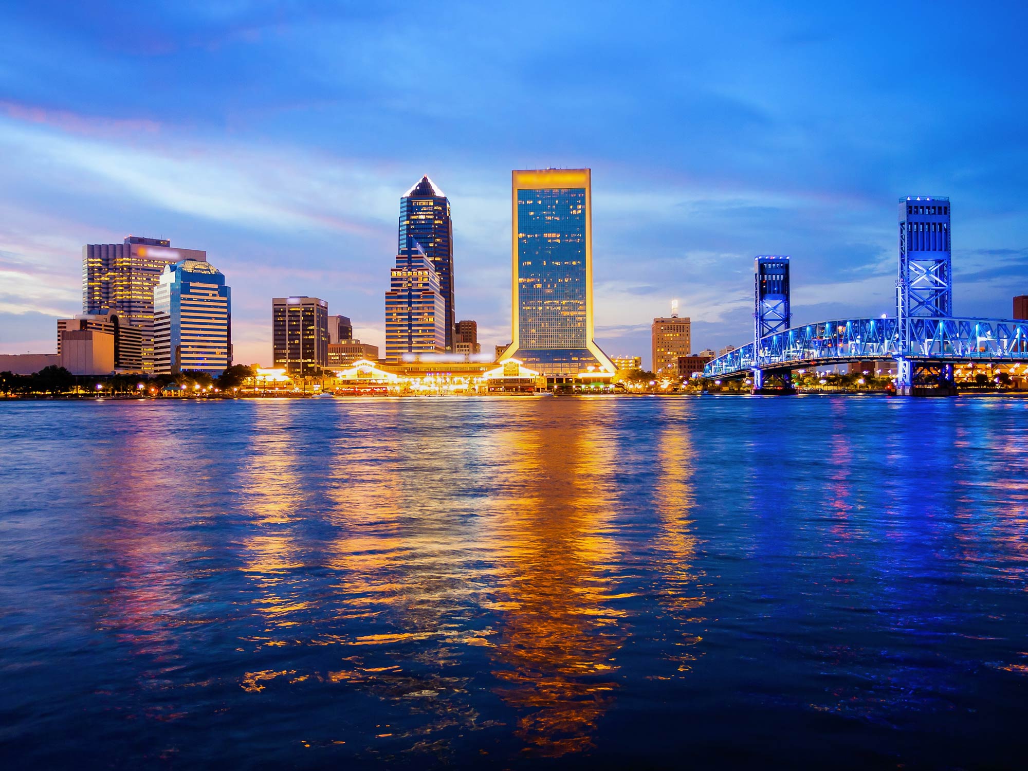 A view Jacksonville, Florida's city skyline over the St. John's River at night with a bridge on the right of the image