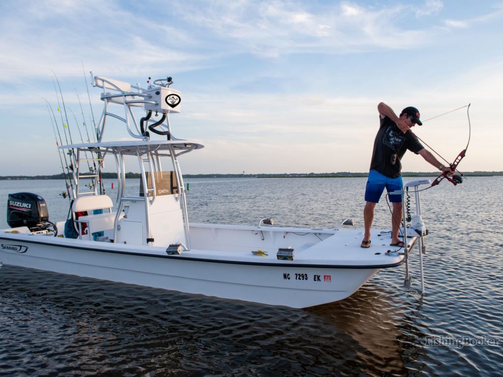 A bowfisher aiming his recurve bow from a boat.