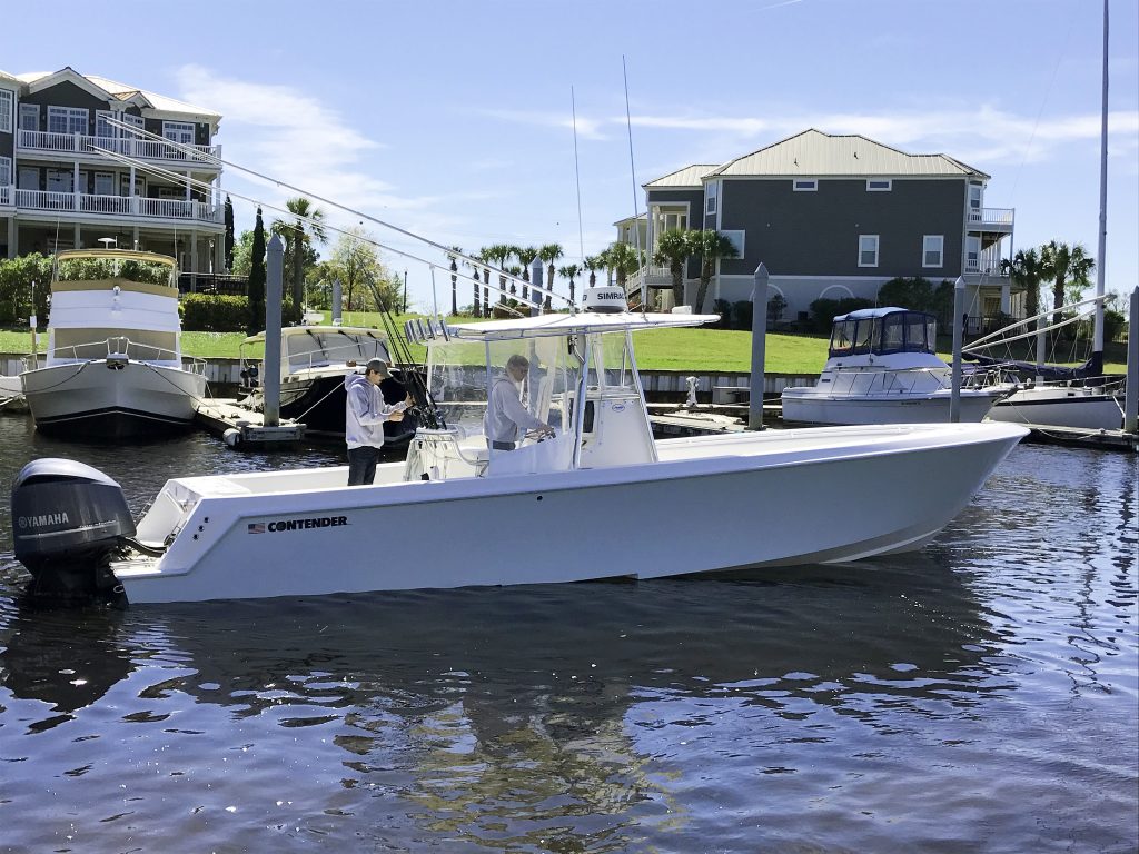 A center console fishing boat moored near Myrtle Beach, with two men on it, and houses in the background 