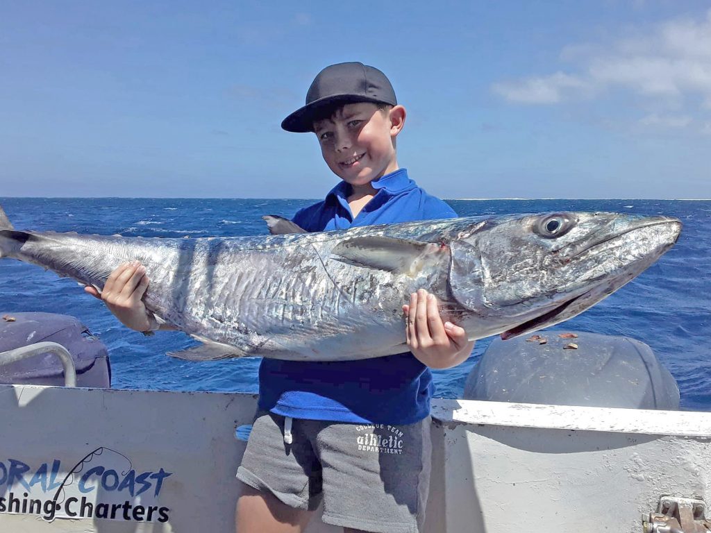 A happy child holding a huge Mackerel with blue skies and water in the background