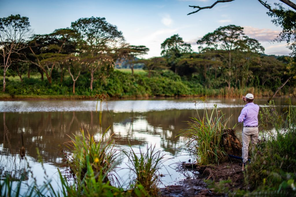 an angler holding a fly fishing rod on a river bank in Kenya