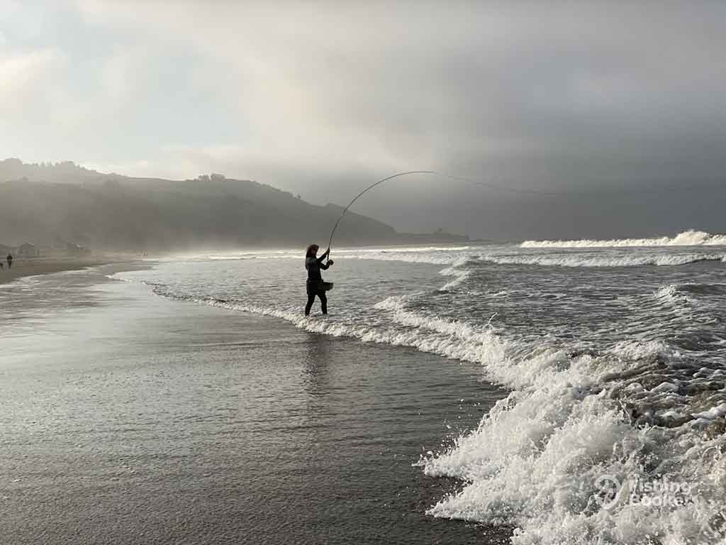 A view along a beach in Richmond, CA, on a blustery day towards a lone angler casting a line into the surf, with the waves crashing in from the right of the image