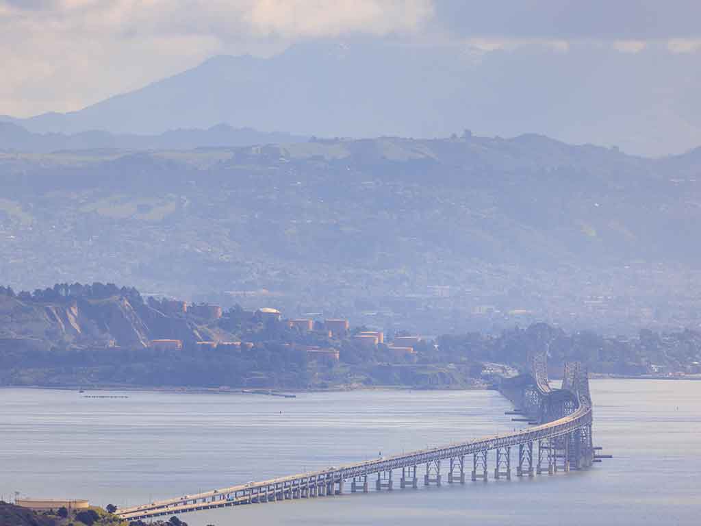 An aerial view looking towards the San Rafael Bridge in Richmond, CA, on a hazy day, with a mountain visible in the distance beyond some residential buildings
