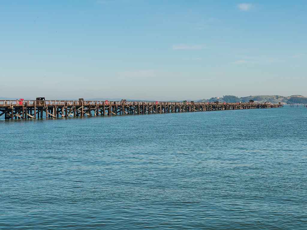A view across the water towards a long but shallow fishing pier in the San Francisco Bay on a sunny day