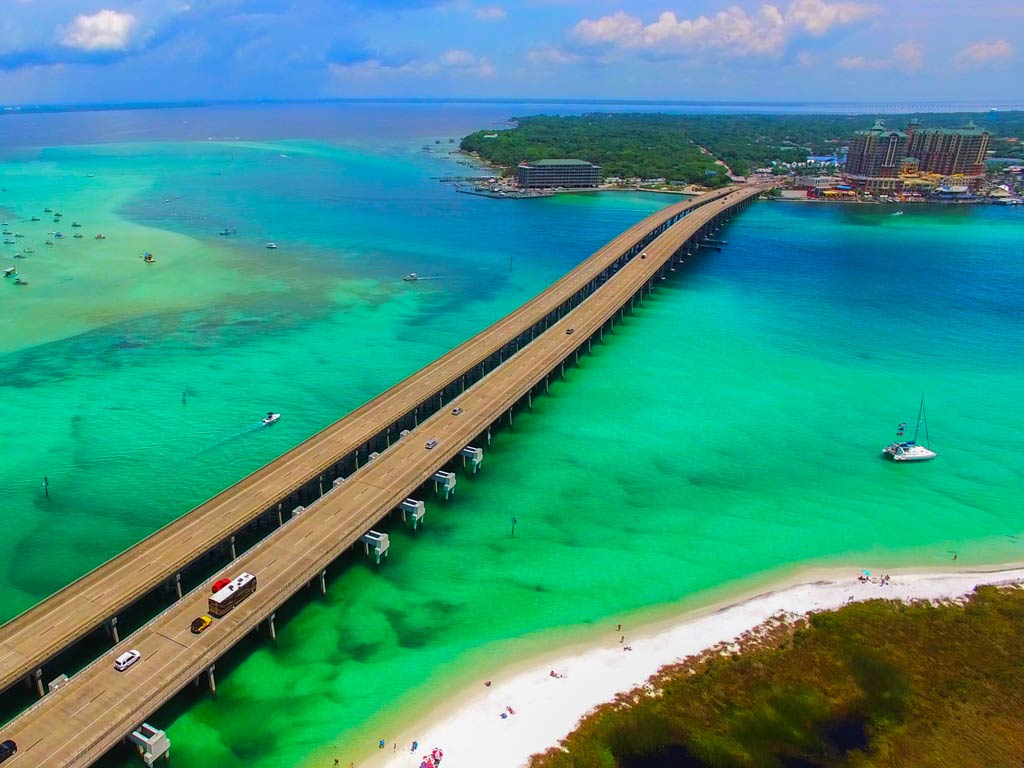 An aerial photo of a bridge and blue-emerald waters near Eglin Beach in Destin, Florida, with several boats visible in the water.