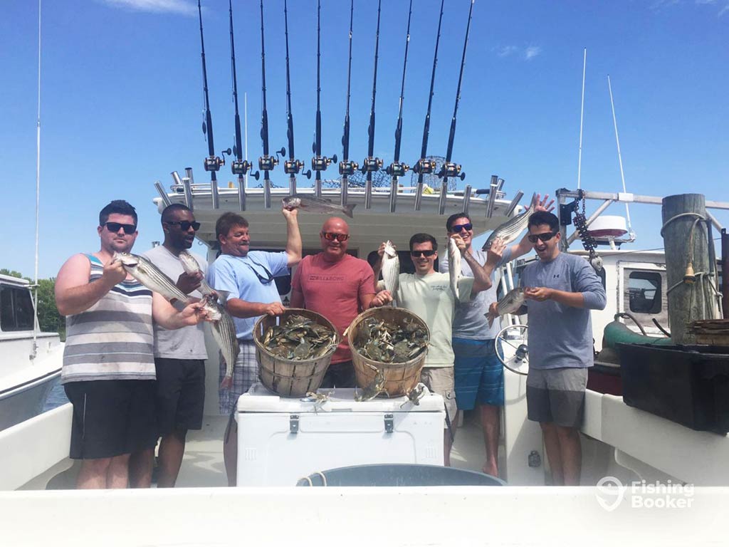 A group of anglers aboard a fishing charter in Baltimore, with trolling rods ready for fishing above their heads, holding up two nets full of Crabs, along with a couple of other fish on a clear day